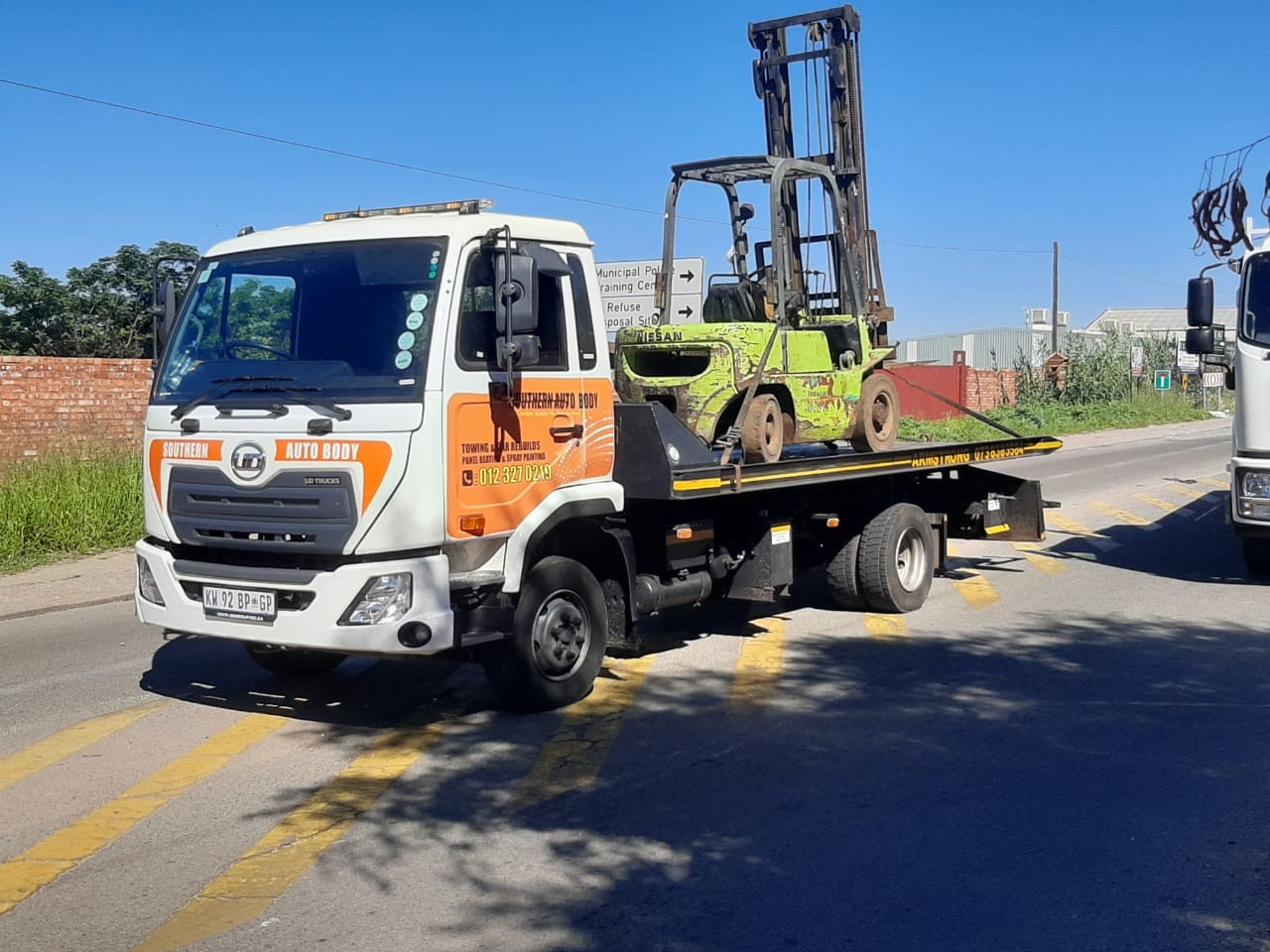 Armstrong Towing flatbed tow truck carrying a forklift on the road